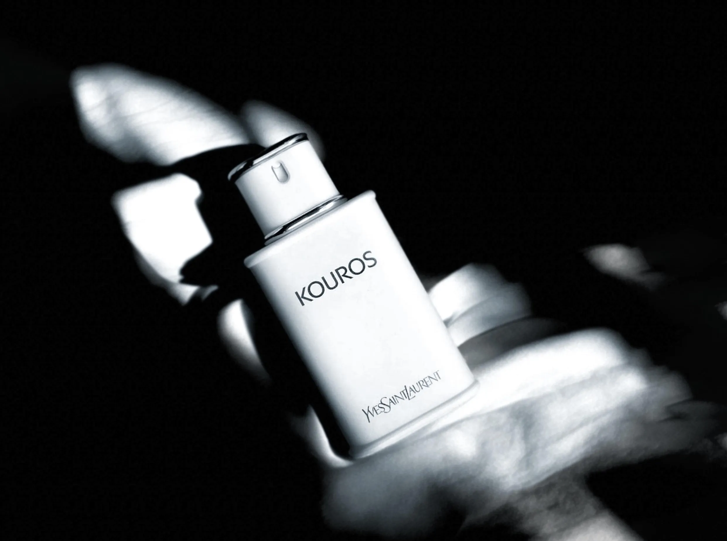 A white bottle of Yves Saint Laurent Kouros lit dramatically against a dark background.